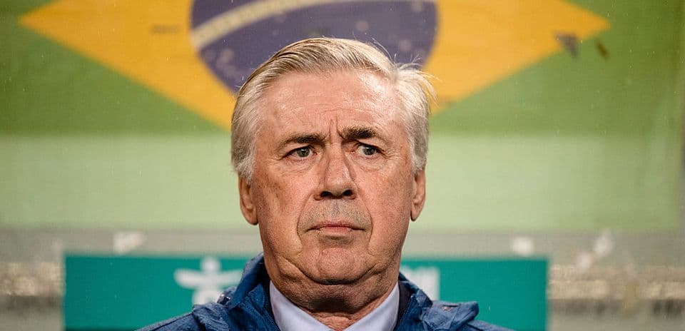 Entrenador con chaqueta itau frente a bandera brasileña