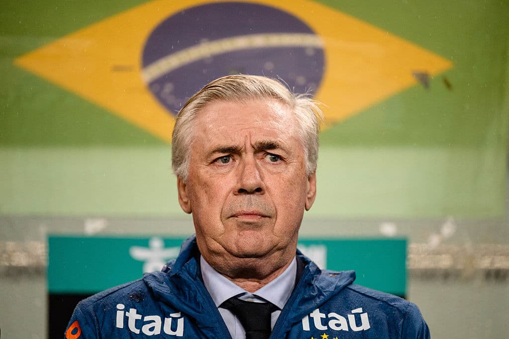 Entrenador con chaqueta itau frente a bandera brasileña