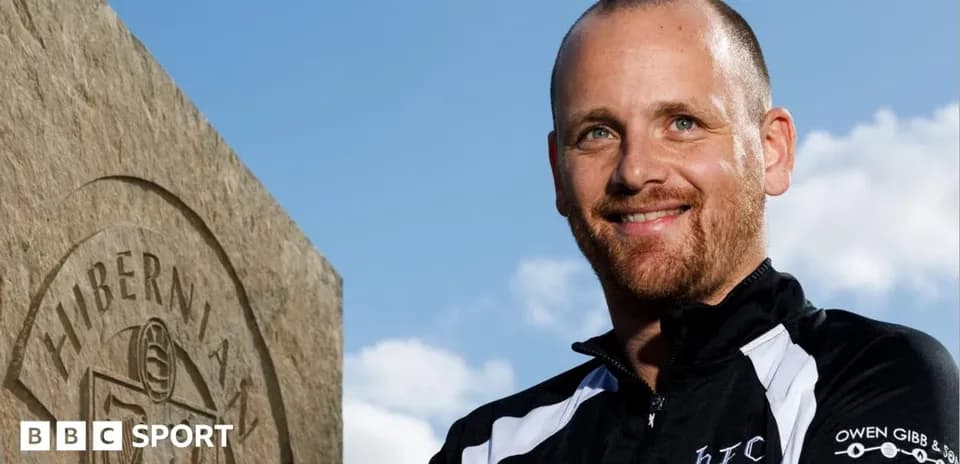 Entrenador posando junto a una piedra con logo