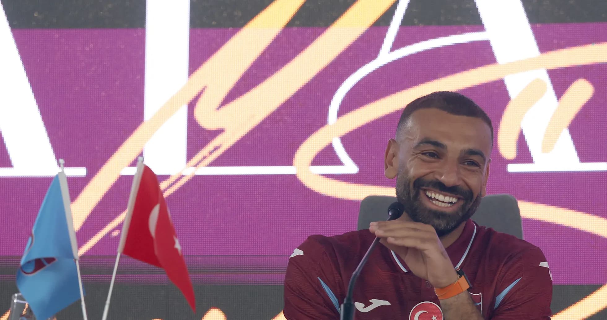 Jugador sonriente en conferencia de prensa con banderas