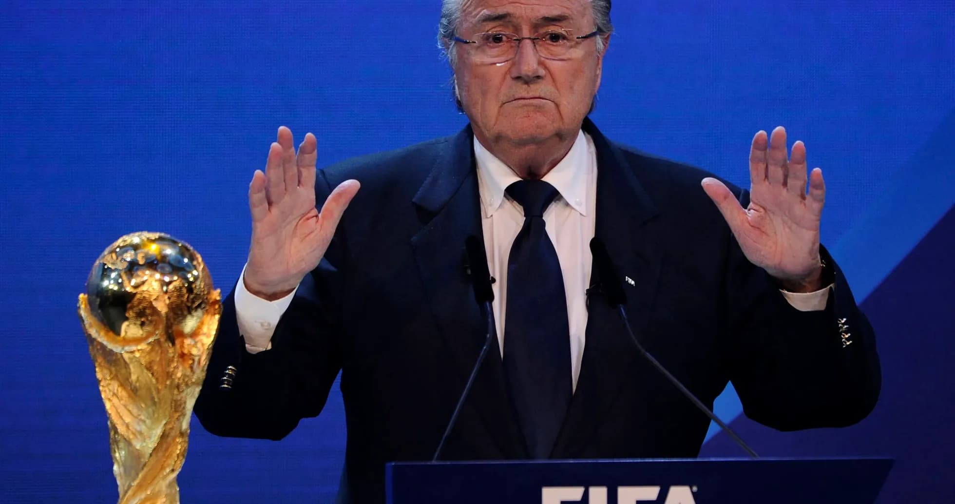 Hombre hablando en conferencia de FIFA con trofeo