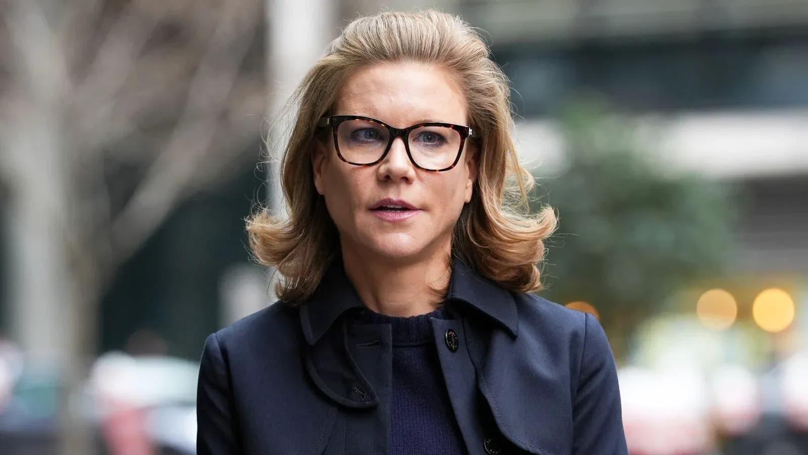 Mujer con gafas y abrigo oscuro caminando al aire libre