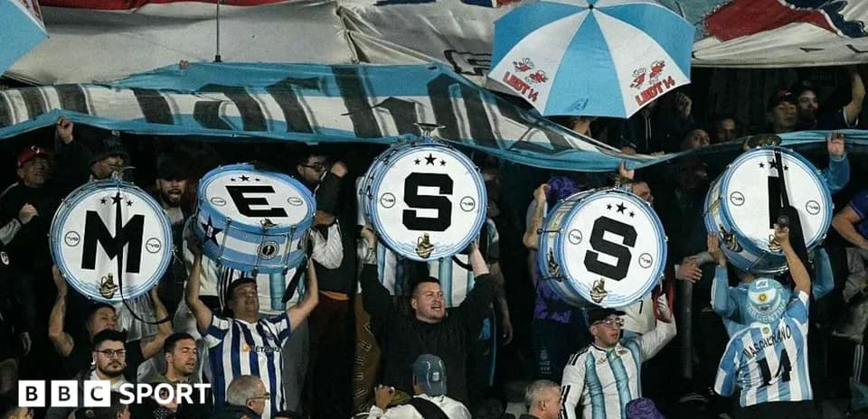 Aficionados sosteniendo tambores con letras en un partido