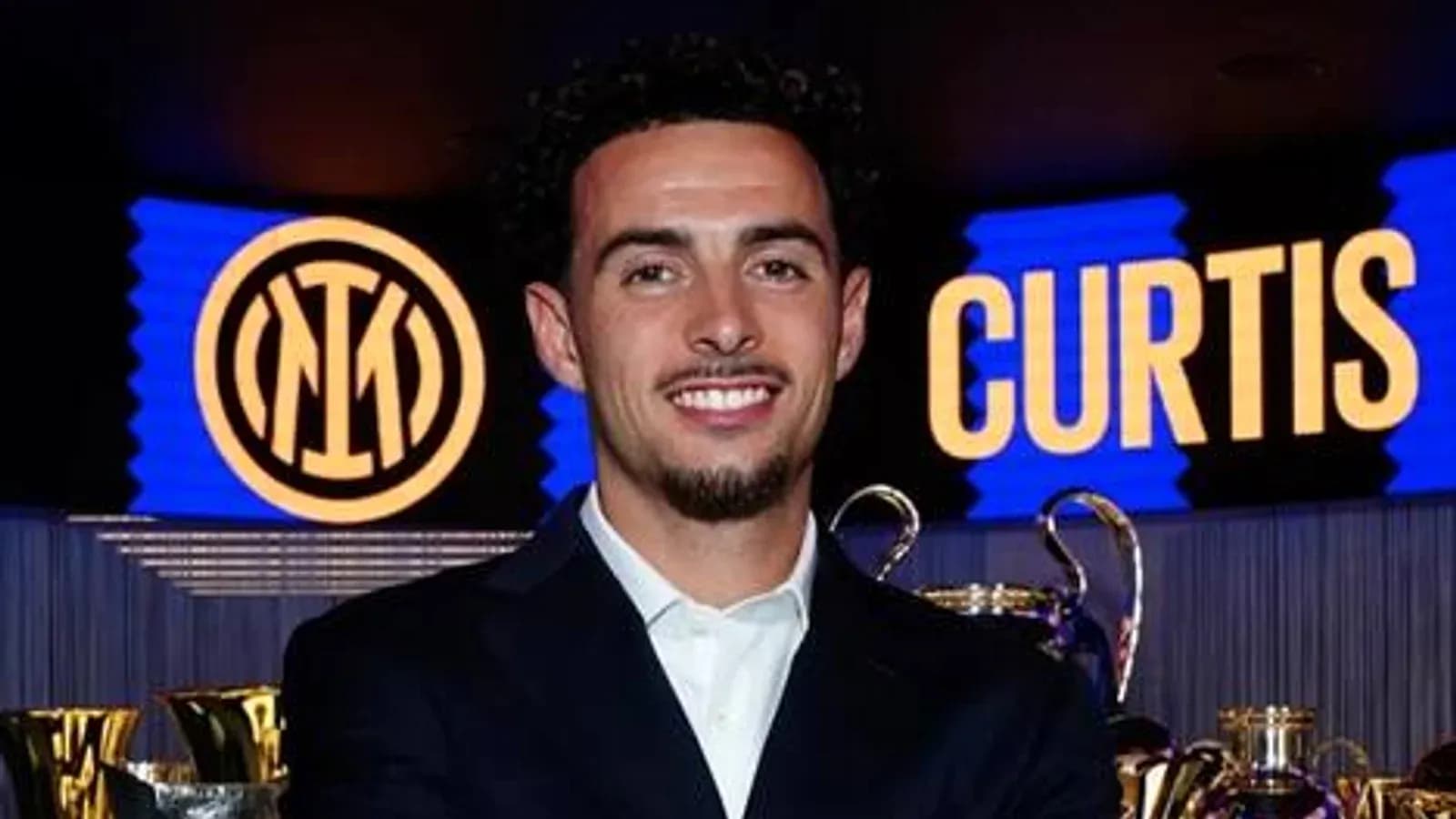 Jugador posando frente a trofeos y logo de Inter Jugador posando frente a trofeos y logo de Inter